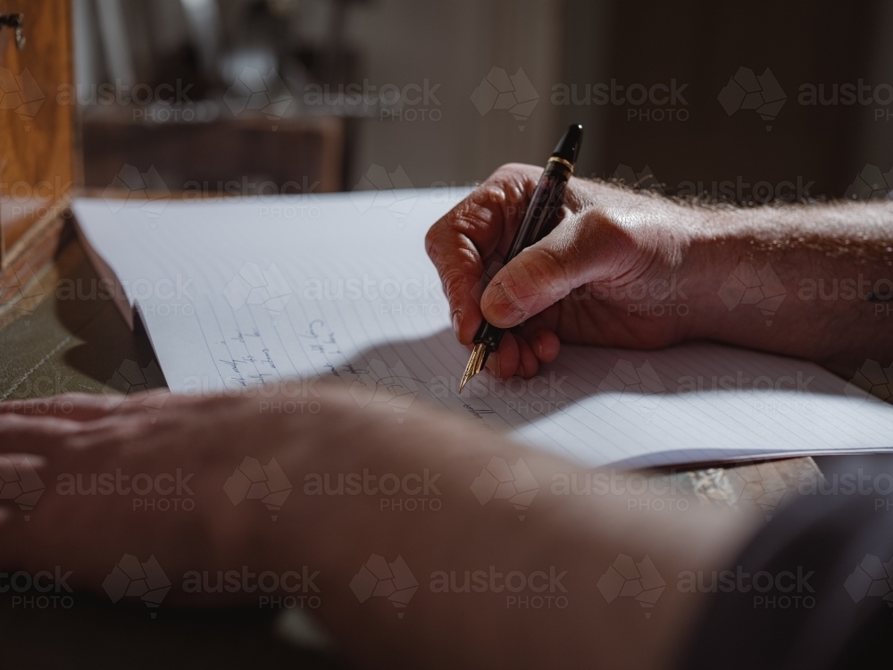 A person's hand holding a pen and writing on a lined notebook - Australian Stock Image