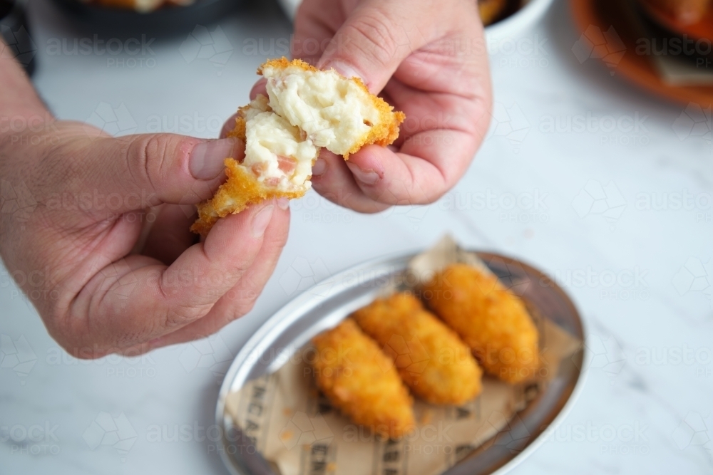 Hands breaking open fried food - Australian Stock Image