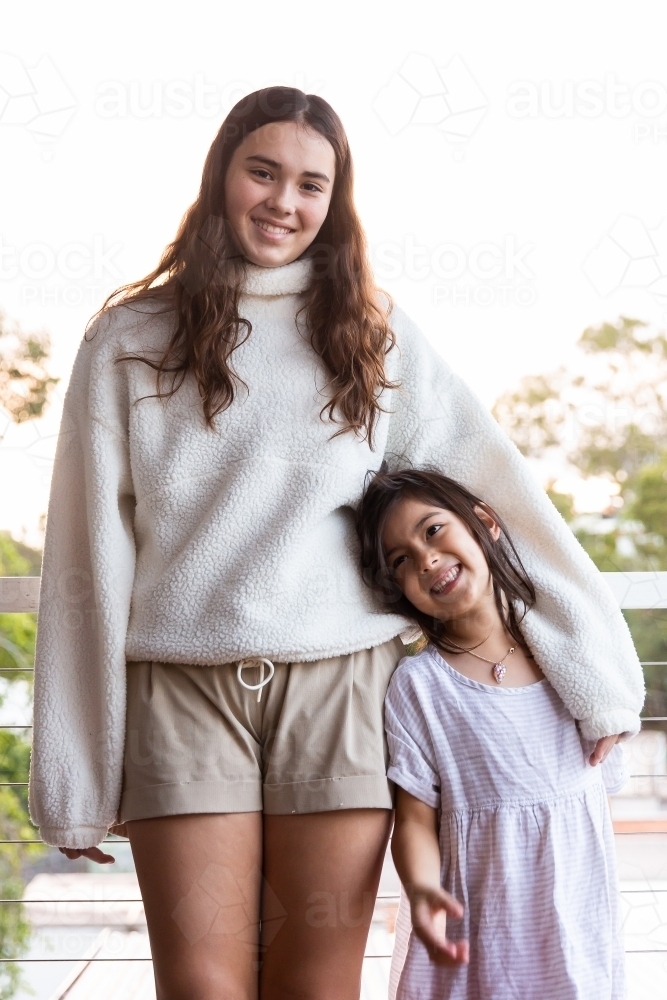 Close-up photo of two sisters standing smiling while looking at the camera - Australian Stock Image