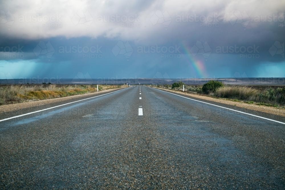 A rainbow and rain falling from a cloud over a road - Australian Stock Image