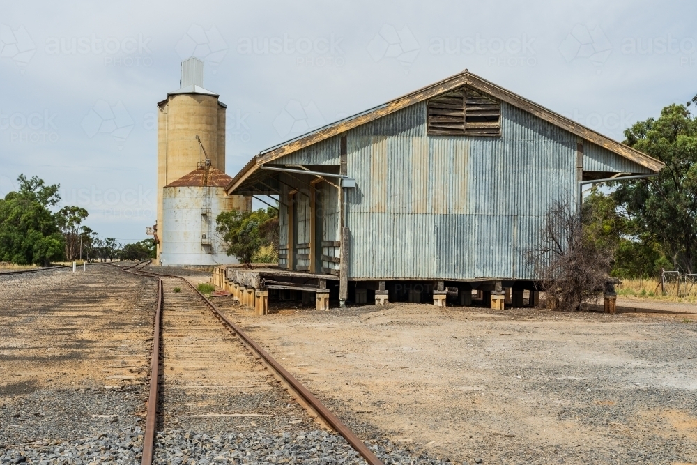 A regional railway line running past an abandoned tin goods shed and wheat silos - Australian Stock Image