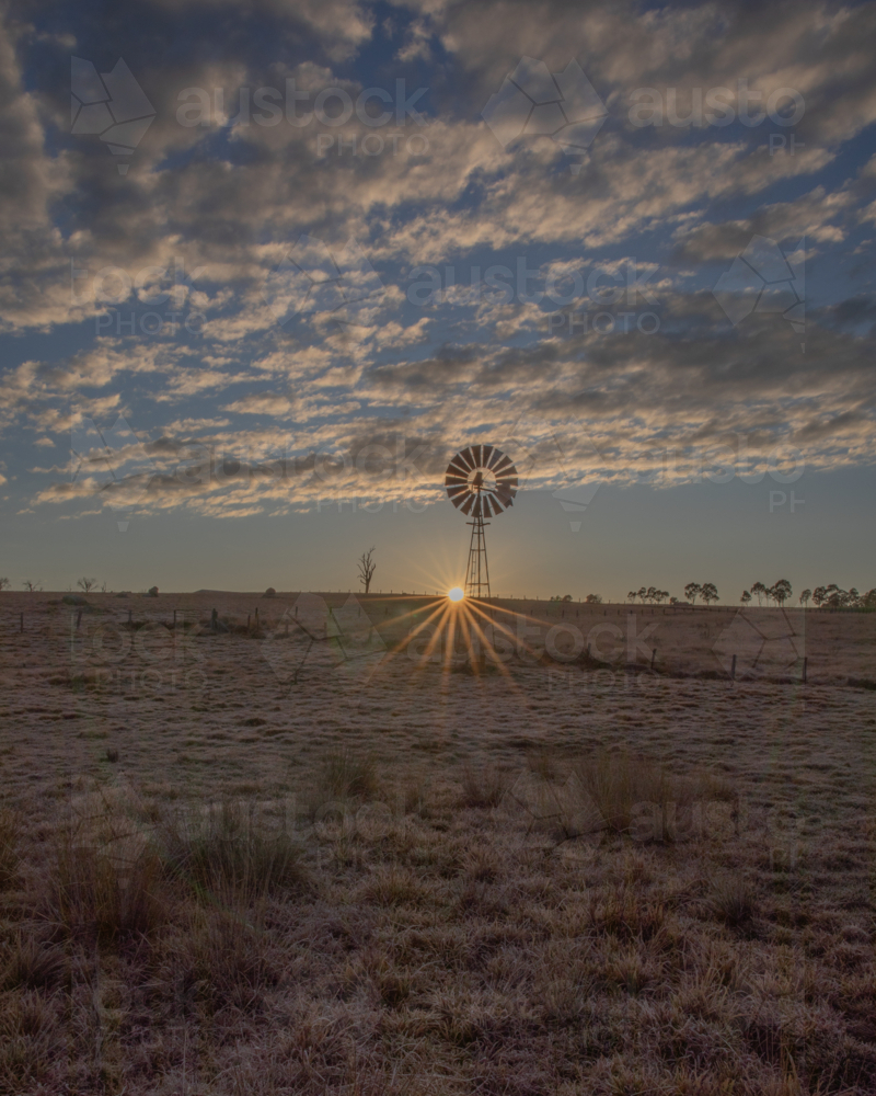 A rising sun, a country windmill and a cloudy sky - Australian Stock Image