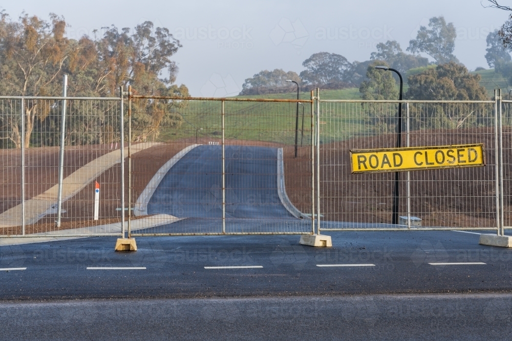 A road closed sign hanging on a fence block a brand new seal road - Australian Stock Image