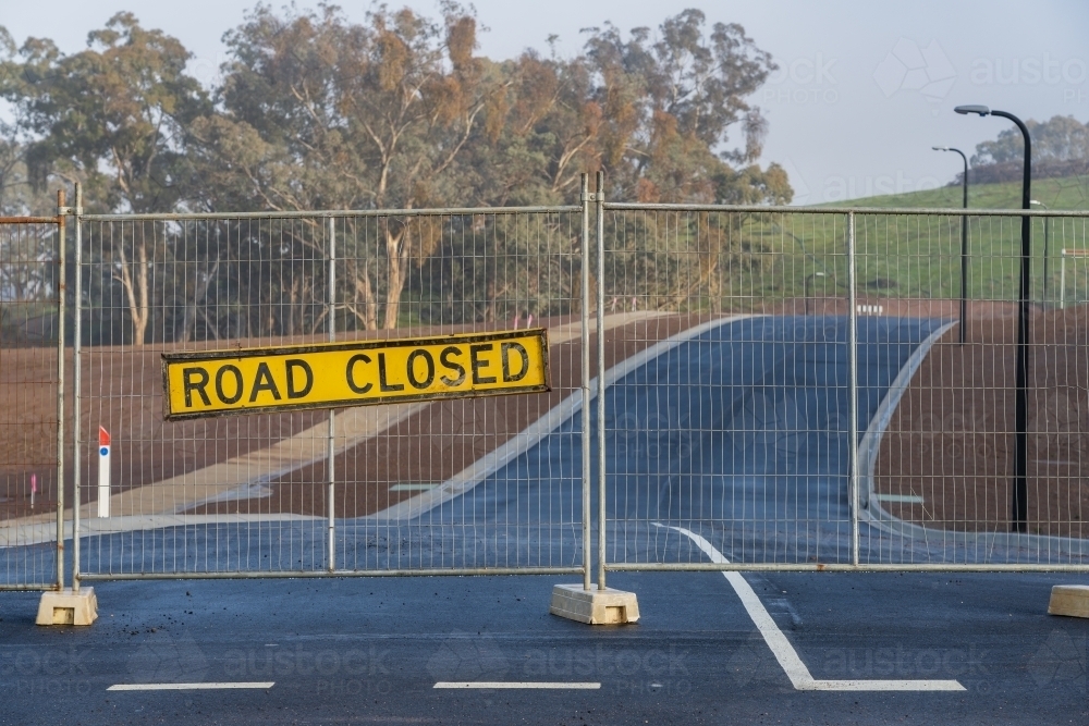 A road closed sign hanging on a fence block a brand new seal road - Australian Stock Image