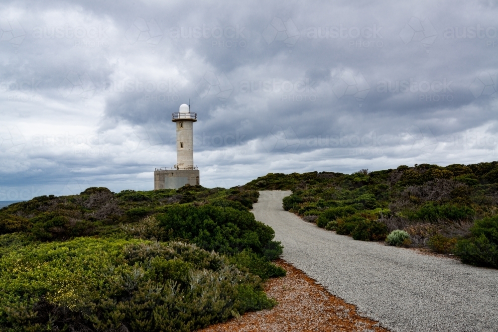 A road leading up to a lighthouse through low growing shrubs with stormy sky - Australian Stock Image