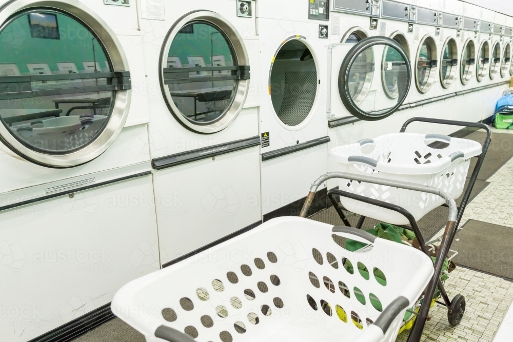 A row of tumble dryers in a launderette with washing carts in front - Australian Stock Image