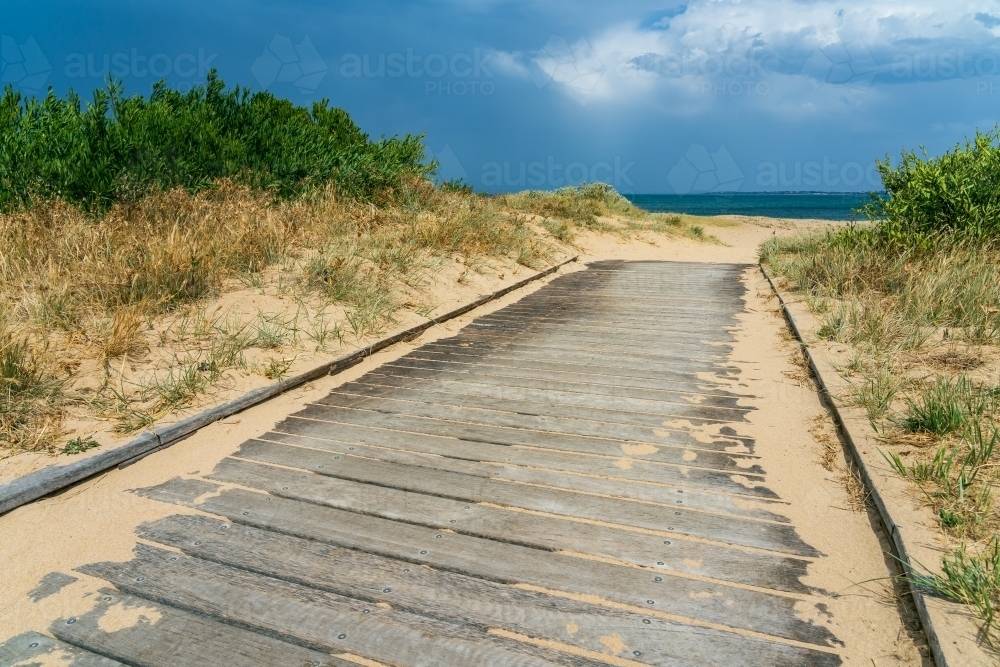 A sandy coastal boardwalk leading towards a dark sky - Australian Stock Image