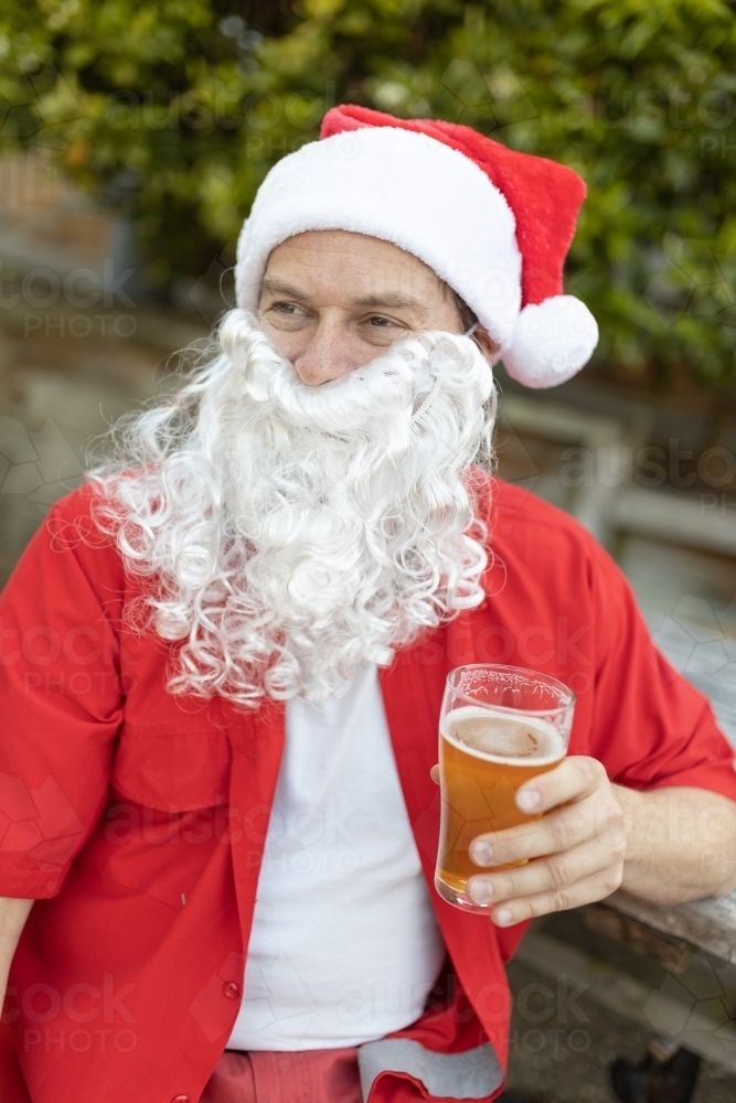 A Santa Claus at Christmas time in  the Australian summer holding a beer - Australian Stock Image