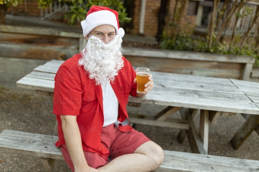 A Santa Claus at Christmas time in  the Australian summer holding a beer - Australian Stock Image