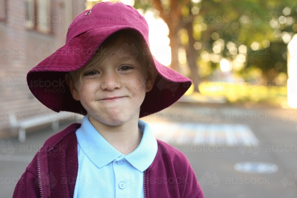 A school boy wearing his school hat grinning while standing outside - Australian Stock Image