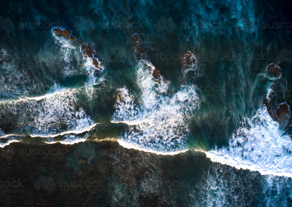 A series of waves pass exposed rocks in the ocean - Australian Stock Image