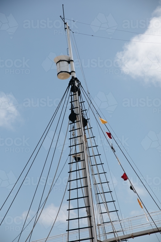 A ship's mast with signal flags at the top and lines of ropes. - Australian Stock Image