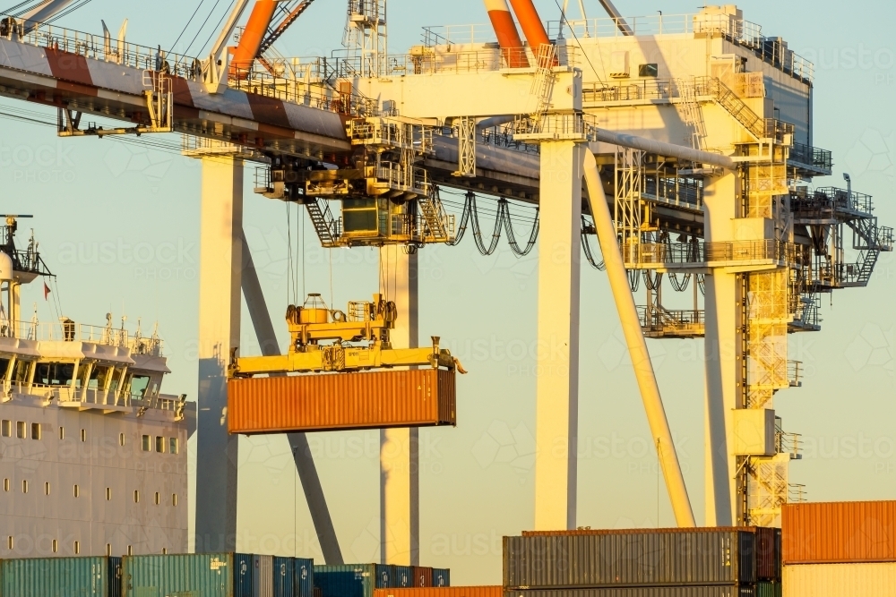 A shipping container hanging from a large crane over a cargo ship ship - Australian Stock Image