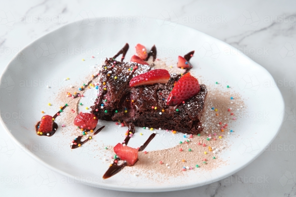 a slice of brownie with chocolate drizzle and topped with sprinkles and strawberry slices - Australian Stock Image