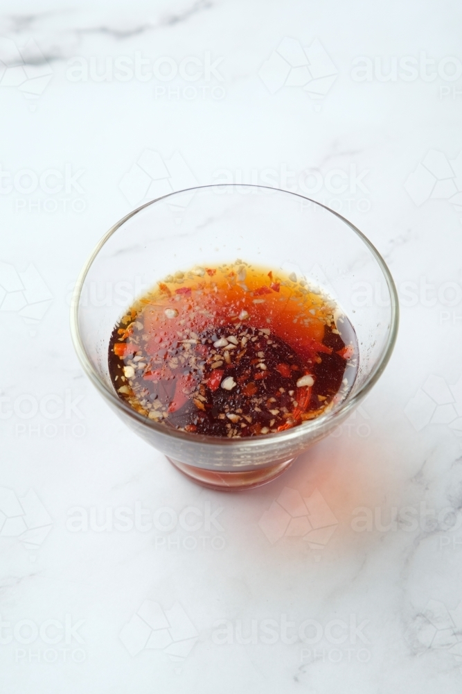 a small glass bowl with dark red sauce and spices - Australian Stock Image