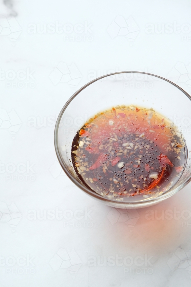 a small glass bowl with dark red sauce and spices - Australian Stock Image