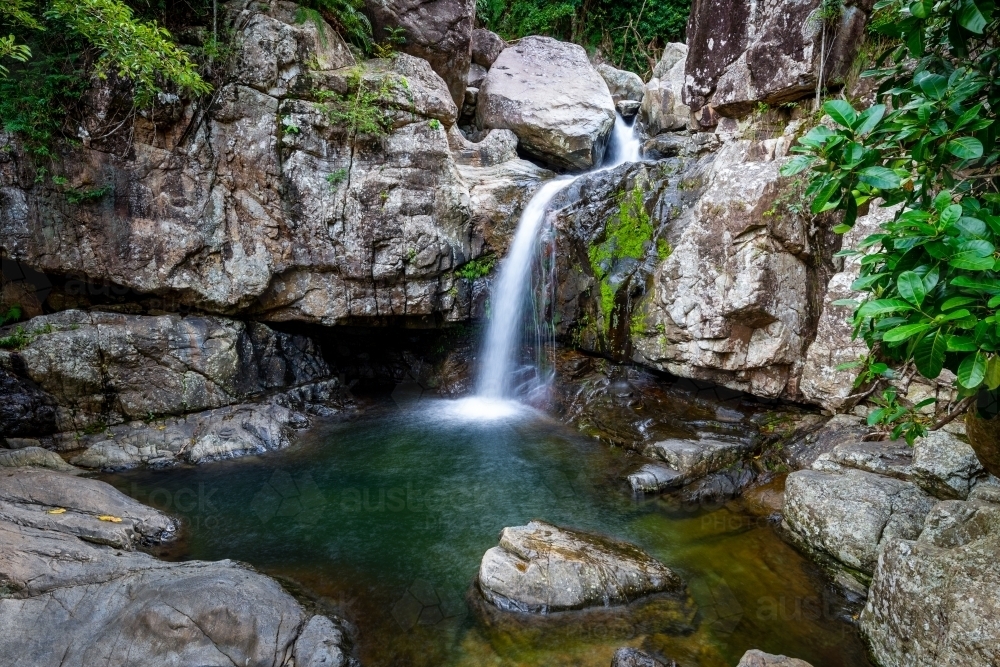 A small waterfall surrounded by large smooth rocks - Australian Stock Image