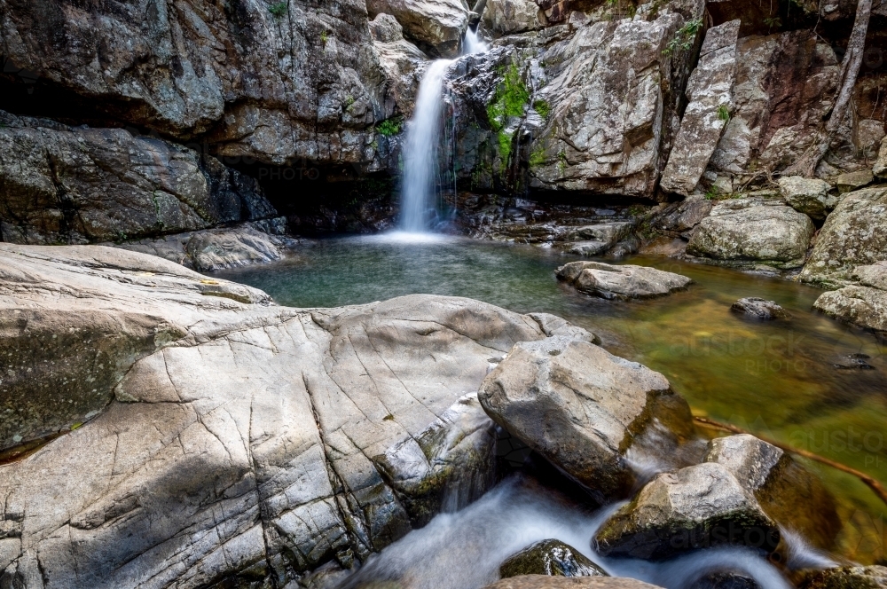 A small waterfall surrounded by large smooth rocks - Australian Stock Image