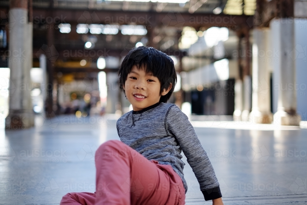 a smiling happy kid sitting on an empty industrial space - Australian Stock Image