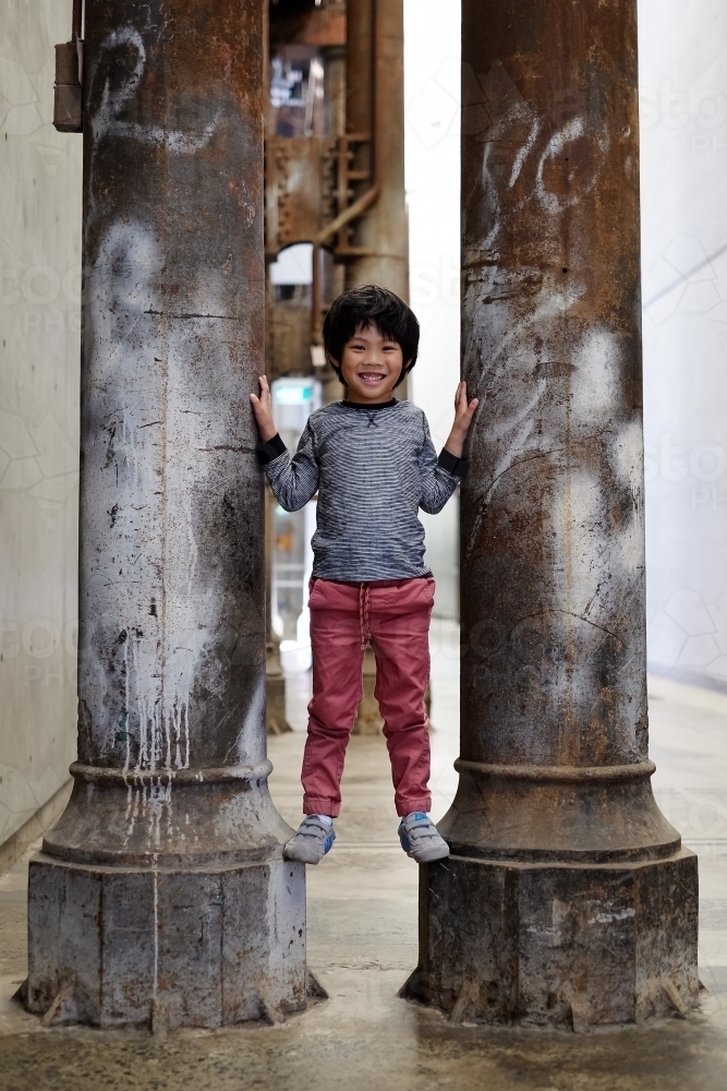 a smiling happy kid standing between two pillars - Australian Stock Image