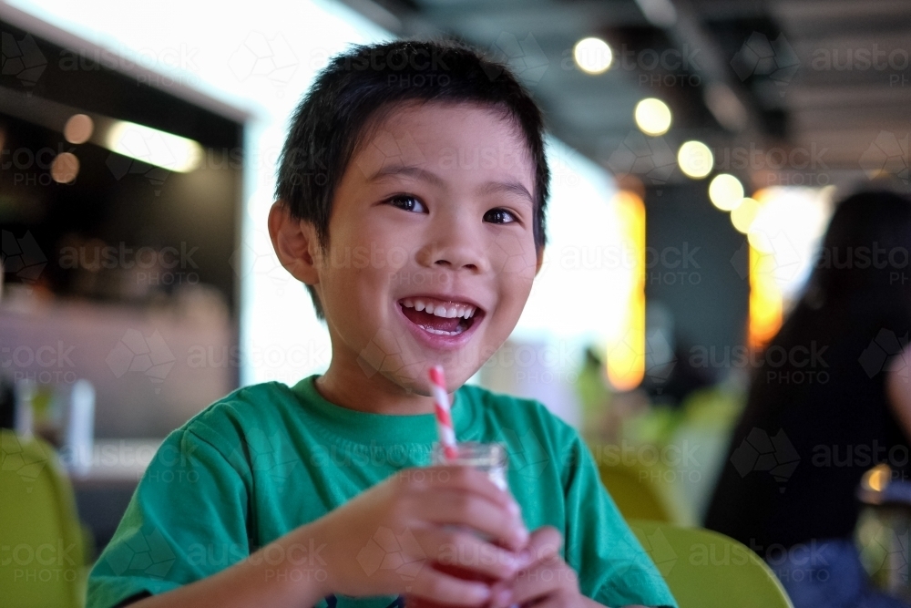 a smiling kid, enjoying a drink at a cafe - Australian Stock Image