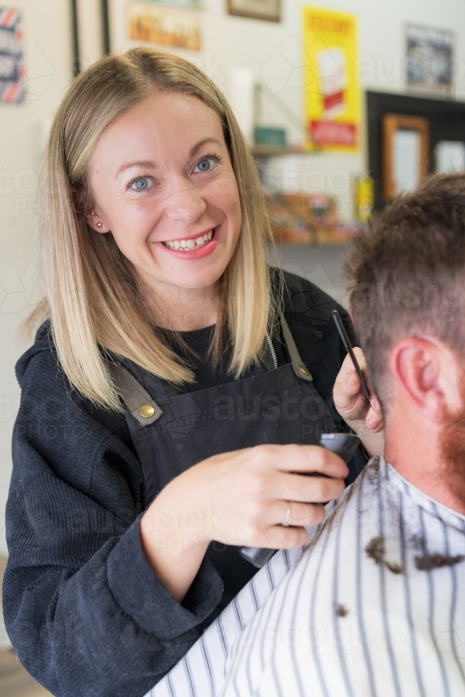 A smiling woman barber trimming hair off the back of a man's neck - Australian Stock Image