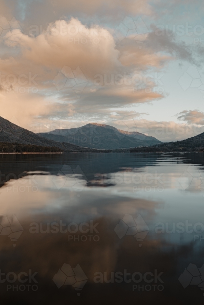 A smooth, still lake with mountains in the background at sunset - Australian Stock Image