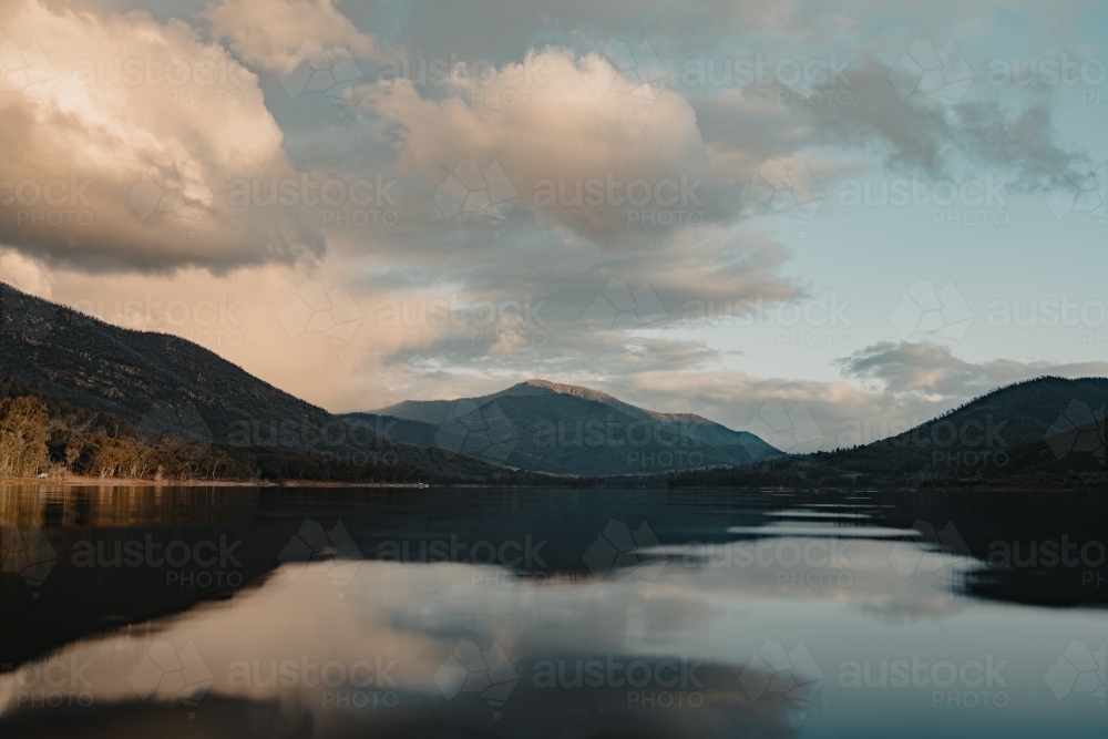 A smooth, still lake with mountains in the background at sunset - Australian Stock Image