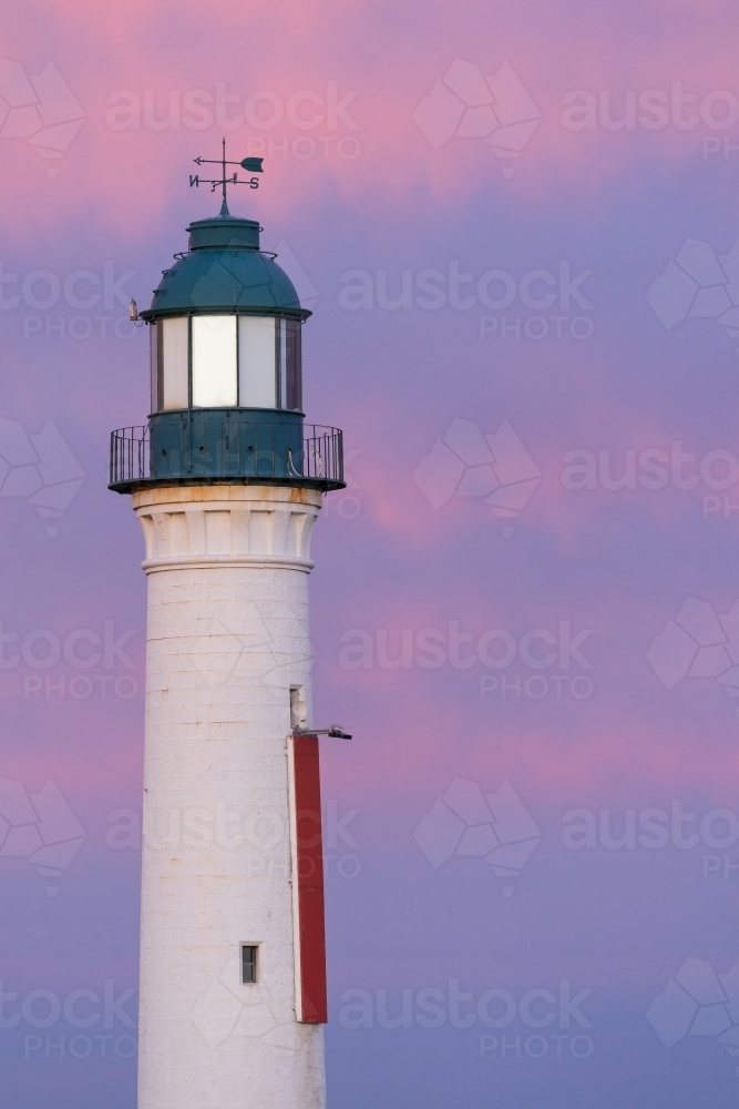 A tall white lighthouse and adjacent light tower against a purple sky at twilight - Australian Stock Image