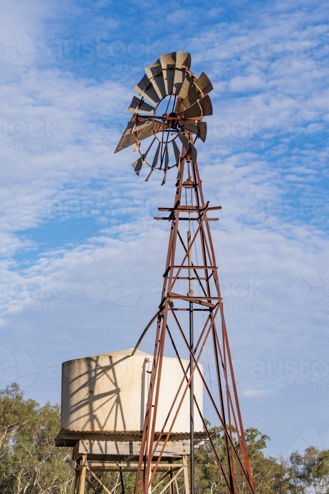 A tall windmill standing next to a water tank - Australian Stock Image