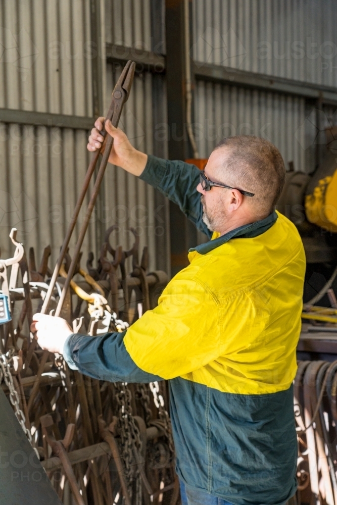 A tradesman wearing high vis clothing lifting a pair of long steel tongs - Australian Stock Image