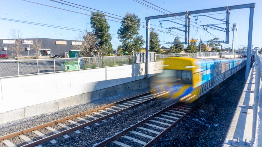 A train moving through a shallow cutting under overhead wires - Australian Stock Image