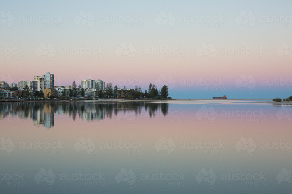 A tranquil waterfront cityscape at twilight, with pastel sky and a reflection of buildings in water - Australian Stock Image