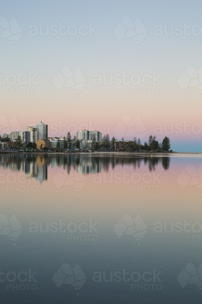 A tranquil waterfront cityscape at twilight, with pastel sky and a reflection of buildings in water - Australian Stock Image