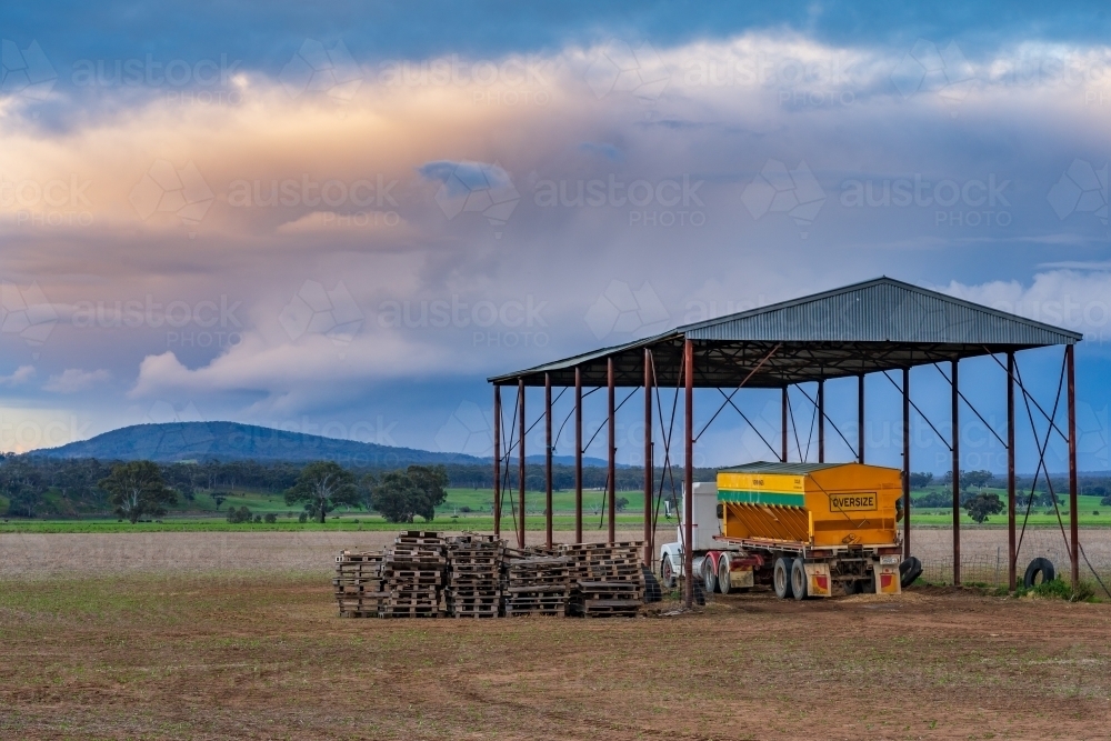 A truck and farm machinery under a hay shed on farmland at sunset - Australian Stock Image