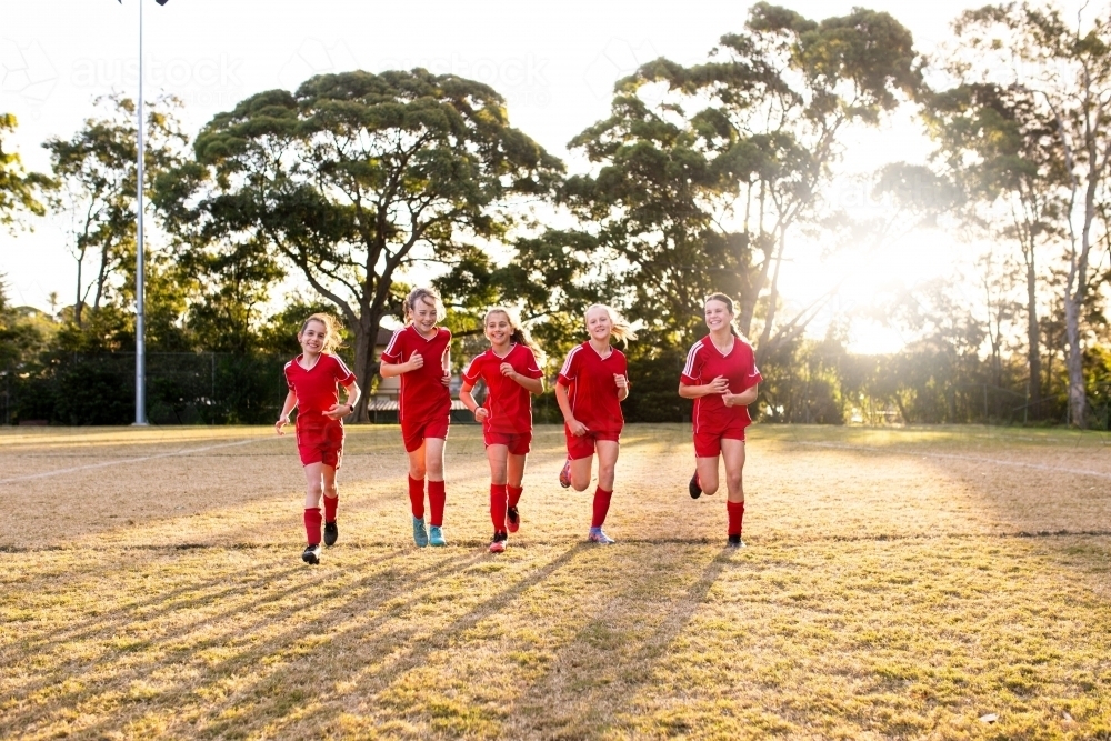 A tween girls football team running towards the camera sports oval - Australian Stock Image