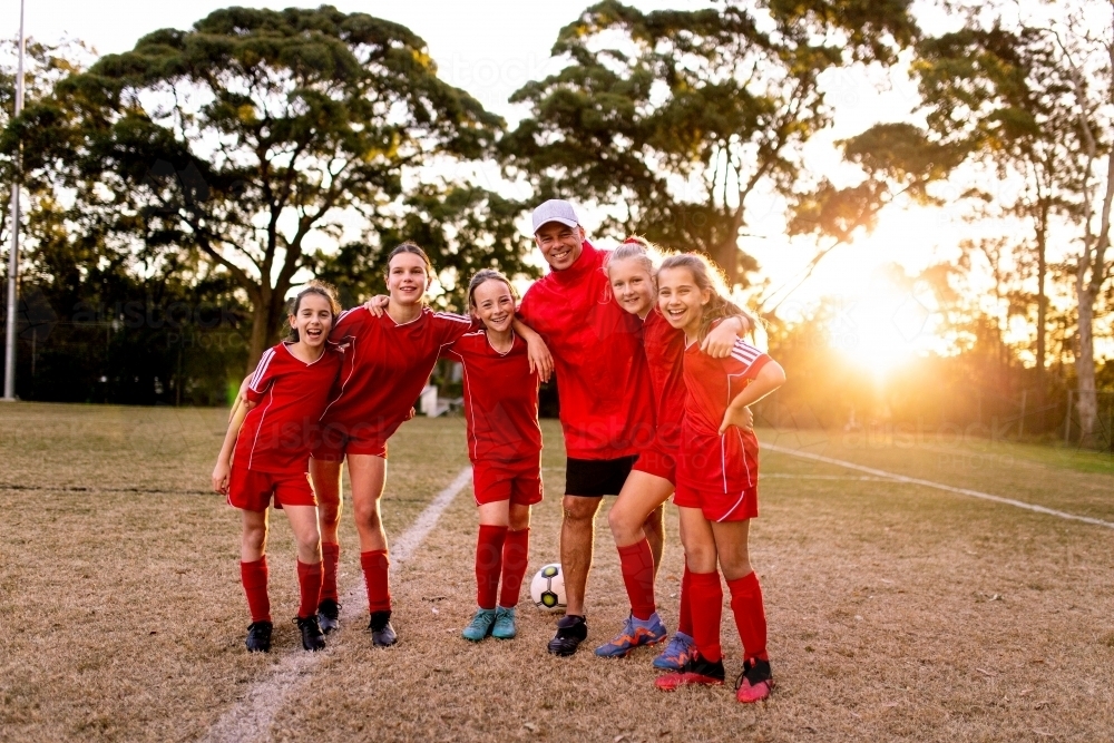 A tween girls football team tmembers walking toward the camera with their coach - Australian Stock Image