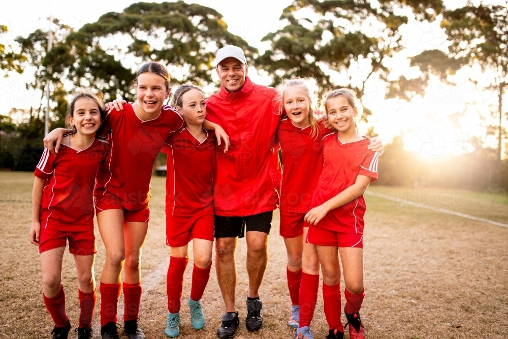 A tween girls football team tmembers walking toward the camera with their coach - Australian Stock Image