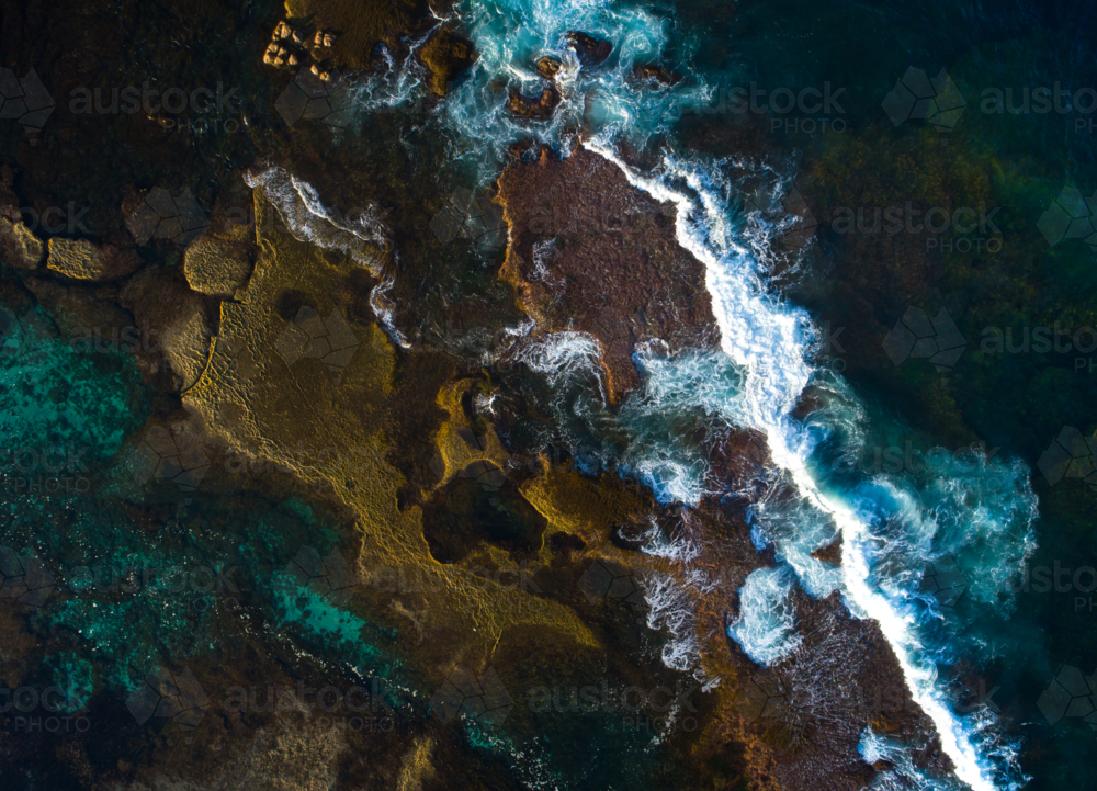 A wave breaks over exposed shapes in a reef bed - Australian Stock Image