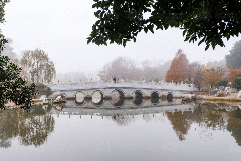 A white, multi-arched bridge crossing over a calm water. - Australian Stock Image