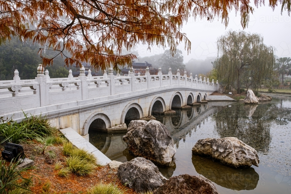 A white, multi-arched bridge crossing over a calm water. - Australian Stock Image