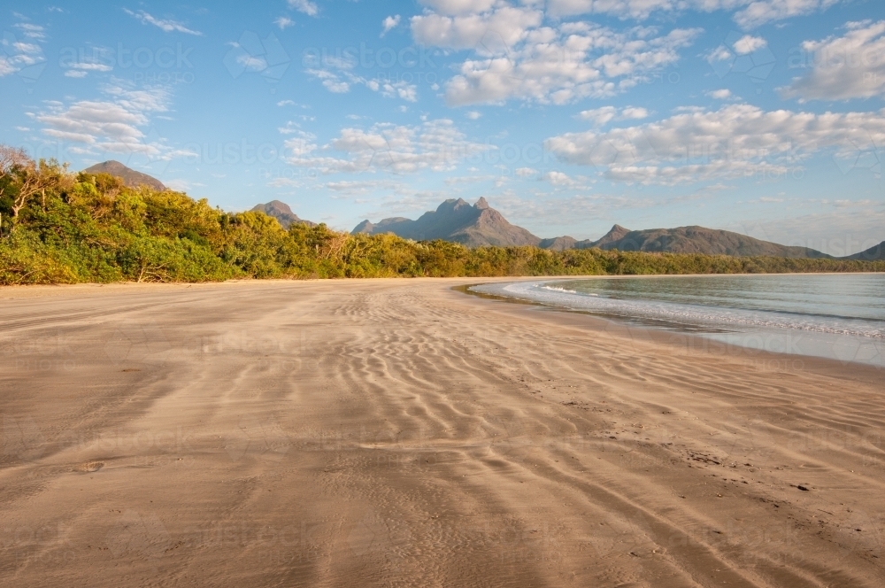 A wide, long beach with mountains in the background taken at dawn - Australian Stock Image