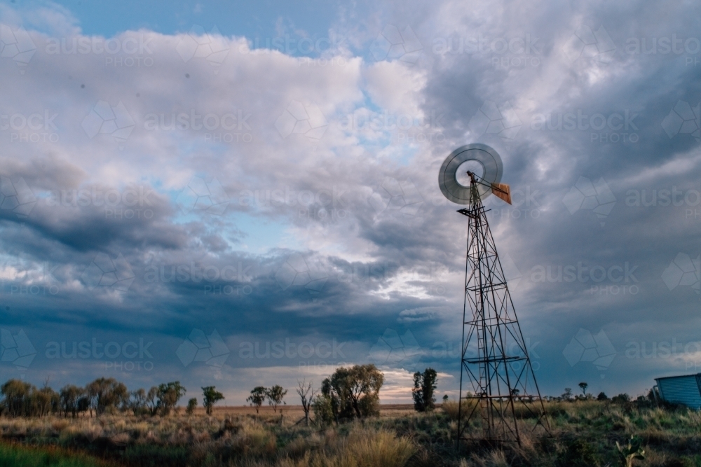 A windmill standing tall against the dark cloudy sky. - Australian Stock Image