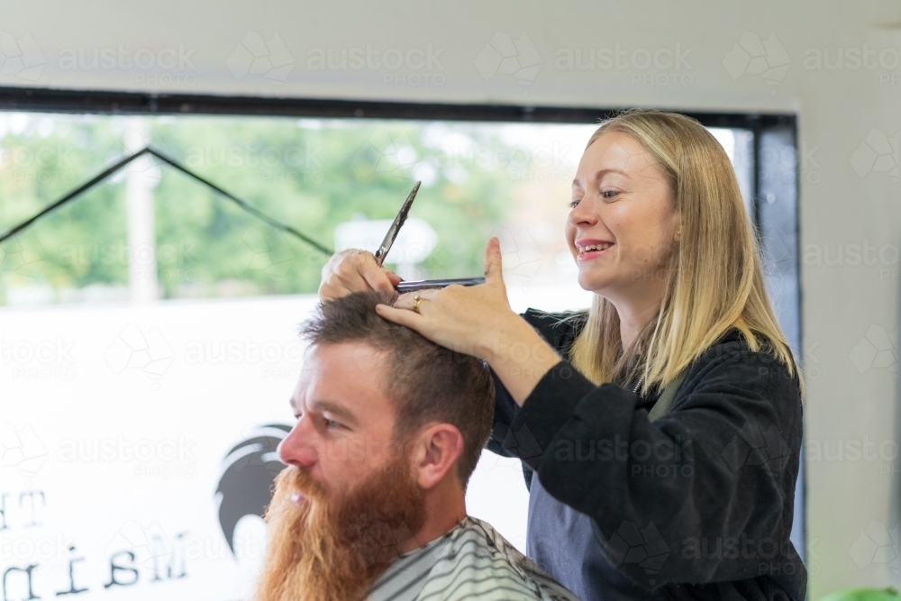 Image of A woman barber giving a haircut to a man with a long beard ...