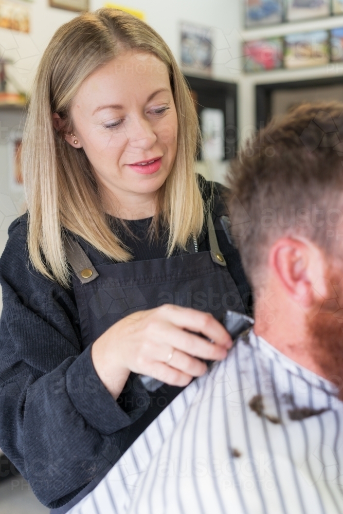 A woman barber trimming hair off the back of a man's neck - Australian Stock Image