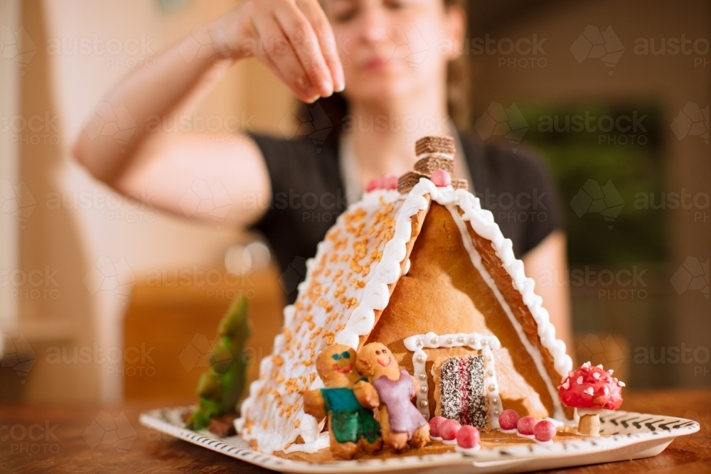 A woman decorating a homemade gingerbread house with figurines - Australian Stock Image