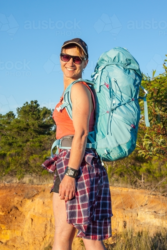 A woman hiker carrying a backpack looking back over her shoulder - Australian Stock Image