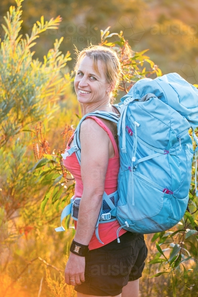 A woman hiker carrying a backpack looking back over her shoulder - Australian Stock Image