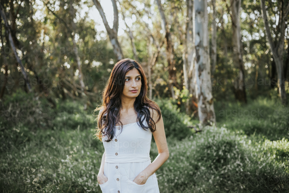 a woman standing amidst a sunlit park forest - Australian Stock Image