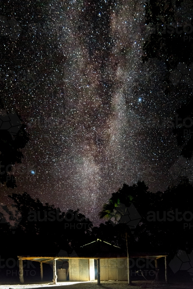 A wooden cabin under the night sky filled with stars. - Australian Stock Image